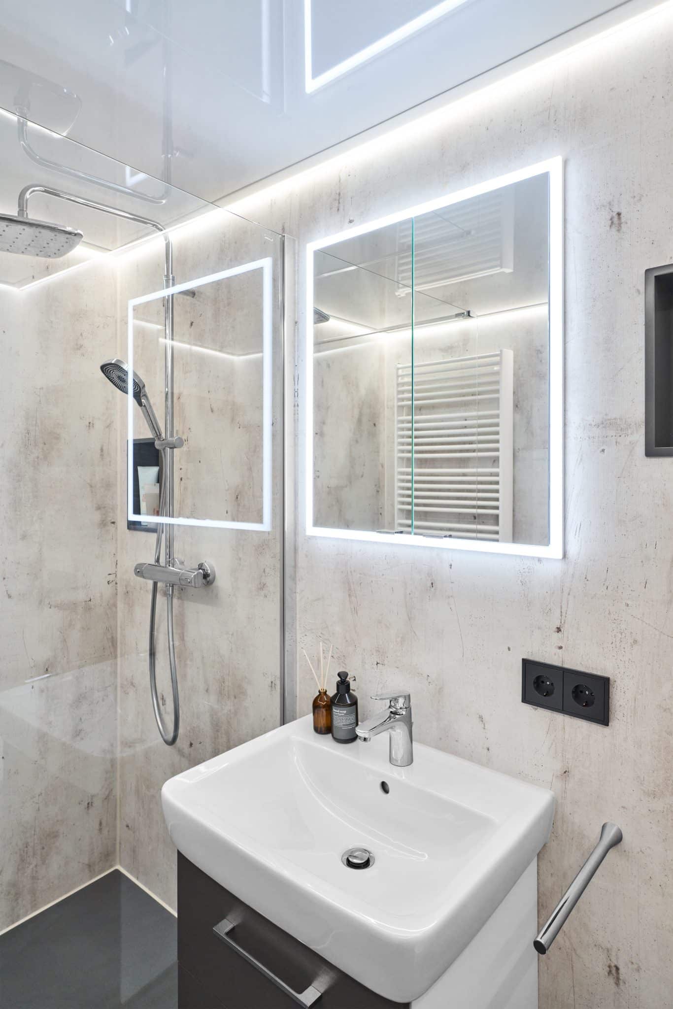 Waschplatz mit beleuchtetem Spiegel neben einer Dusche